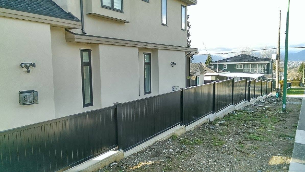 Black aluminum privacy fence on a concrete curb beside a house